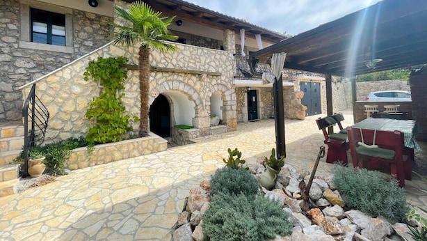 A stone building with a covered patio area, outdoor seating, and a stone staircase. - Villa Paun (Vinodol)