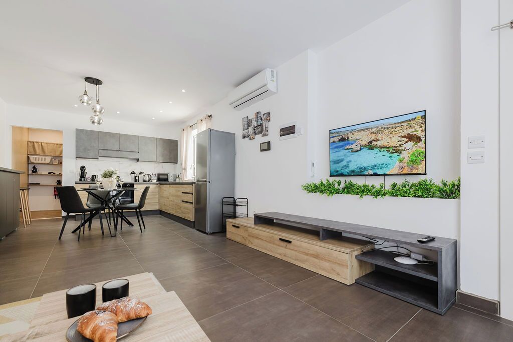 A modern kitchen with grey cabinets, a stainless steel refrigerator, and a dining area with black chairs.