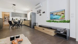 Een moderne keuken met grijze kastjes, een roestvrijstalen koelkast en een eethoek met zwarte stoelen.