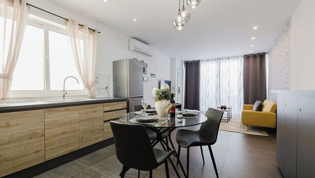 Een moderne keuken met een eethoek, met een ronde tafel, zwarte stoelen en een gele bank in de woonkamer.