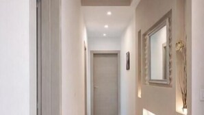 A corridor with a tiled floor, a door at the end, and a wall-mounted mirror with a decorative piece.