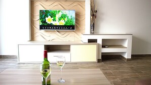 A modern living room with a flat-screen TV mounted on a textured wall, a minimalist entertainment unit, and a wine bottle and glass on a wooden floor.