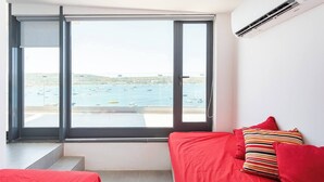 Una habitación con un ventanal grande, una cama con ropa de cama roja y vistas a barcos en el agua.