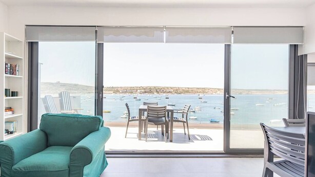 Un balcón con vistas al mar, un sofá color turquesa y una mesa de comedor con sillas.