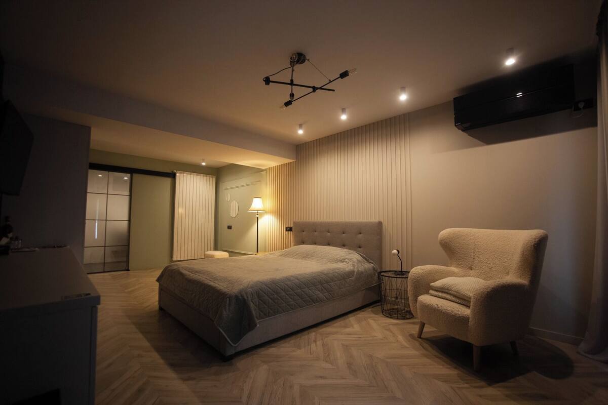 Une chambre à coucher moderne avec un grand lit, une chaise, une table de chevet et un téléviseur fixé au mur.