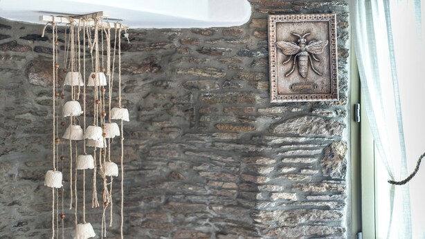A rustic stone wall with a decorative hanging light fixture and a framed bee artwork. - Ifigeneia Luxury Villas (Andros)