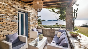 A stone-walled patio with wicker furniture, a hanging light fixture, and a view of the sea. - Ifigeneia Luxury Villas (Andros)
