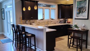 A modern kitchen with dark wooden cabinets, a central island with bar stools, pendant lighting, and a large window.