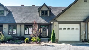 A two-story house with a garage, a front porch, and a small garden with shrubs and a tree.