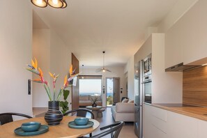 A modern kitchen with a wooden countertop, a dining area with a round table, and a view of the sea through large windows. - KaYa SeaView Residence (Bali)