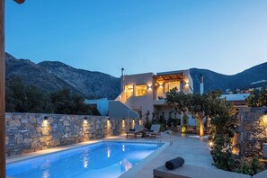 Una casa moderna con piscina, muros de piedra y mobiliario de exterior.