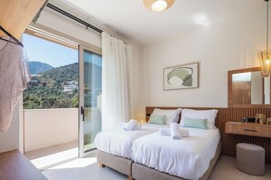 Una habitación de hotel con balcón, cama con sábanas blancas, mesita de noche de madera y un cuadro en la pared.