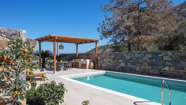 Un área de piscina con pérgola, pared de piedra y mobiliario exterior.