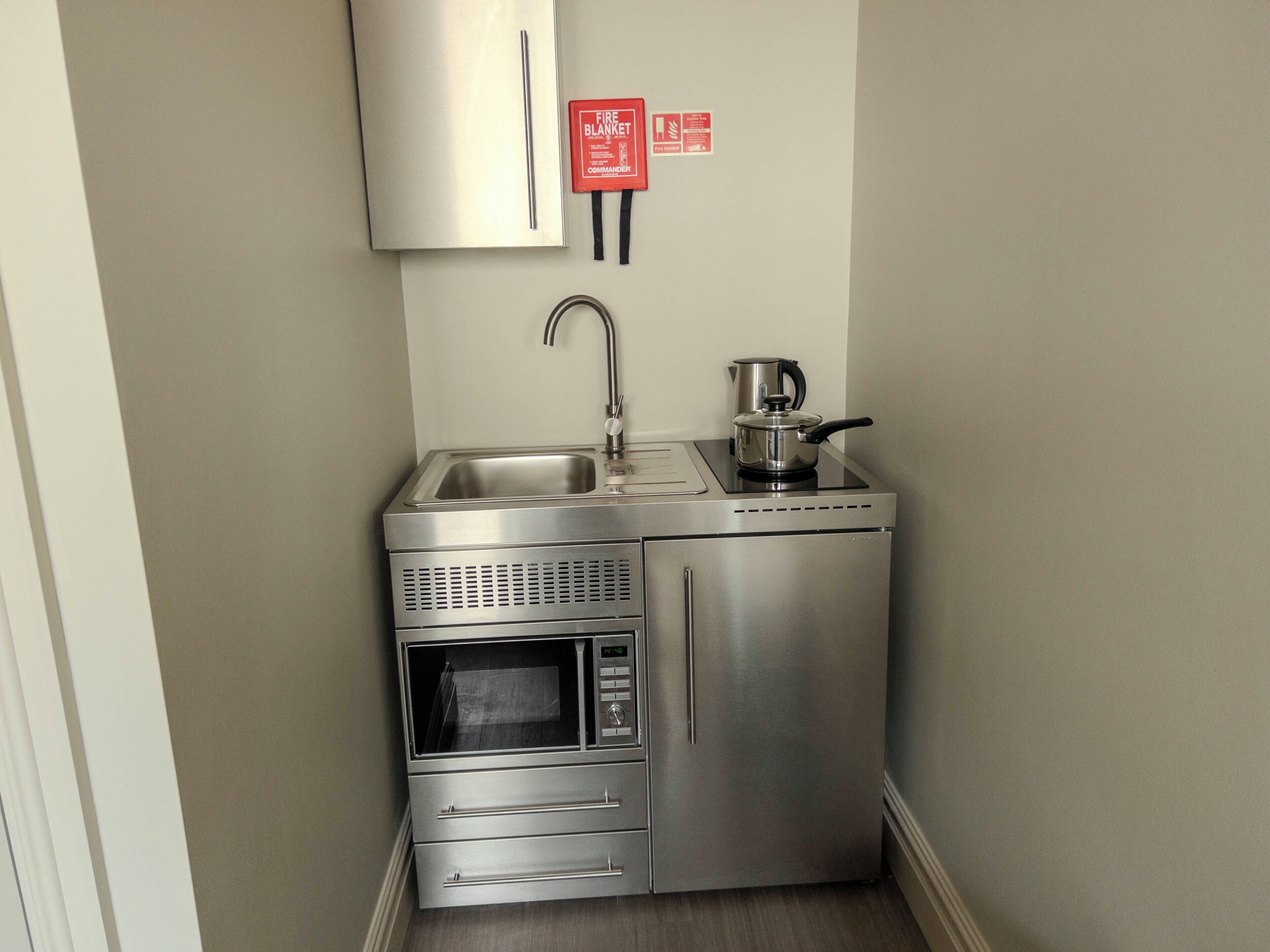 A compact kitchenette with a stainless steel refrigerator, microwave, oven, sink, and a coffee maker.