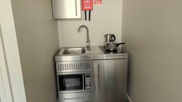 A compact kitchenette with a stainless steel refrigerator, microwave, oven, sink, and a coffee maker.