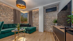 A modern living room with a stone wall, green sofa, wooden floor, and a small round table with a plant. - Villa Giulia Zadarvillas (Privlaka)