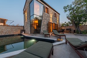Un edificio moderno in pietra con piscina, sedie a sdraio e zona pranzo.