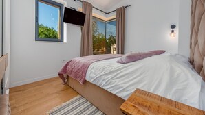 A bedroom with a bed, a TV mounted on the wall, a window, and a ceiling light. - Villa Giulia Zadarvillas (Privlaka)