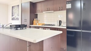 Una cocina moderna con gabinetes de madera oscura, una encimera blanca, una estufa empotrada y un refrigerador negro.