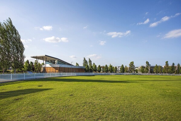 A modern building with a flat roof and large windows, surrounded by a well-maintained lawn and a white fence. - Group Holiday Home Sleeps 12 Penrith Flexible Family and Contractor Stay (Penrith)