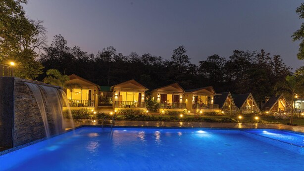 Un resort notturno con piscina, diverse casette e una cascata.