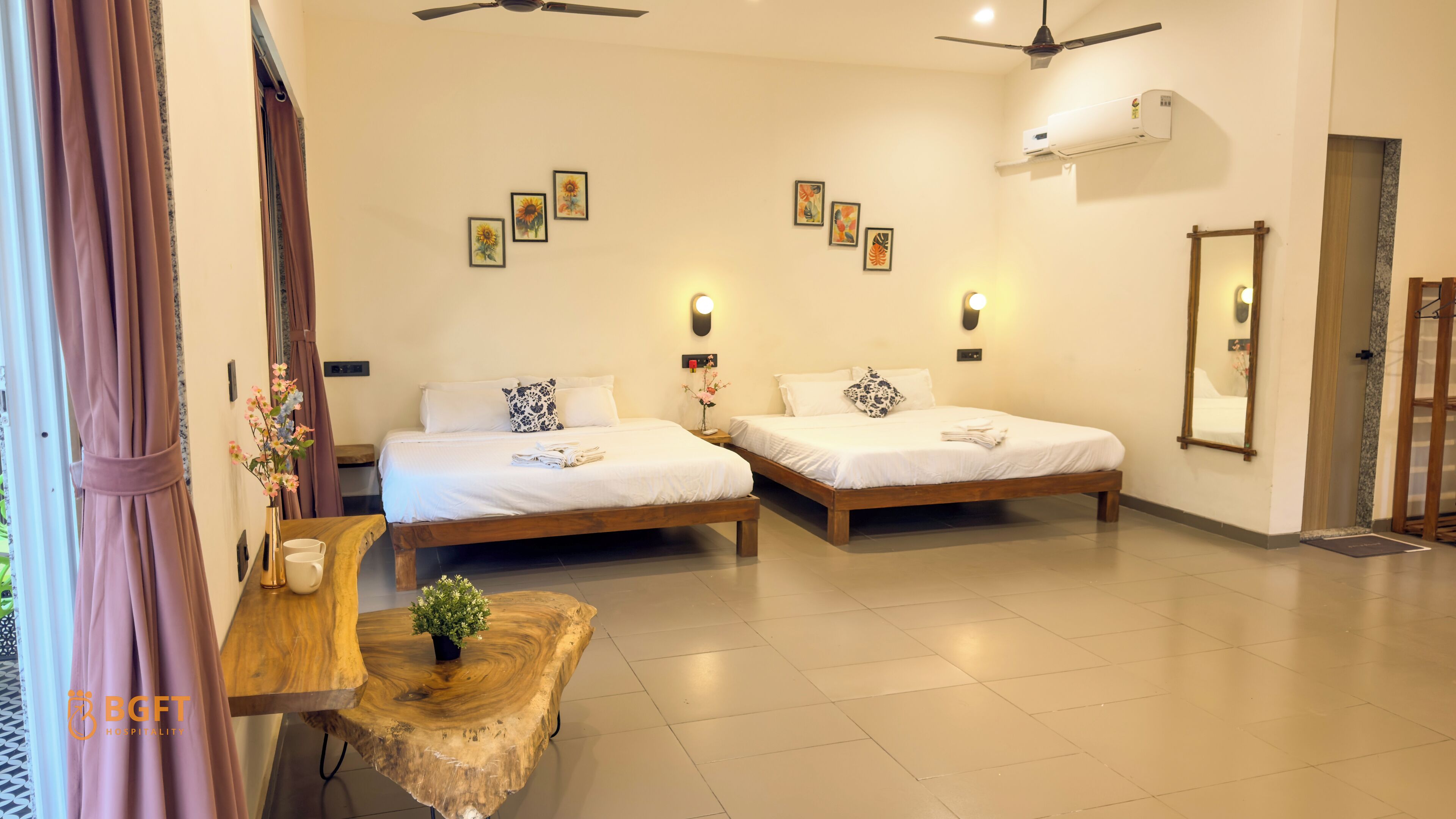 A hotel room with two beds, a wooden coffee table, a vase with flowers, and wall-mounted artwork.