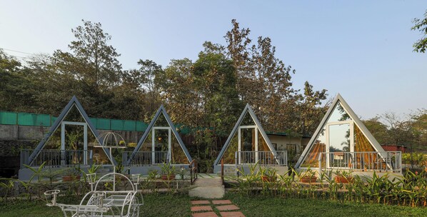Three triangular cabins with glass walls, surrounded by greenery and a stone pathway. - Mountain Woods Farm Stay (Khalapur)