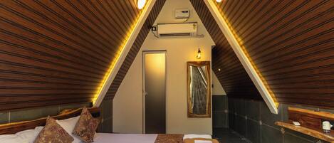 A triangular room with a bed, a mirror, and an air conditioning unit.
