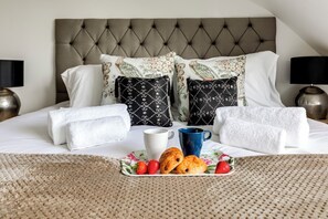 A neatly made bed with a tufted headboard, two pillows with floral and geometric patterns, two white towels, a plate with croissants and strawberries, a white mug, and a blue mug. - Mill Hill Duplex | 3BR · Balcony · London in 28 Mins (London)
