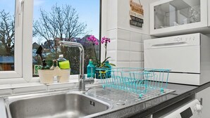 Eine Küche mit Spüle aus Edelstahl, Geschirrgestell und verschiedenen Küchenutensilien auf der Arbeitsfläche.