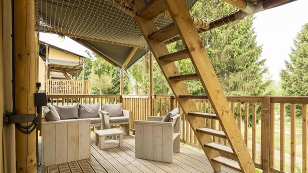 A wooden deck with outdoor seating, a ladder, and a covered area with a mesh roof.
