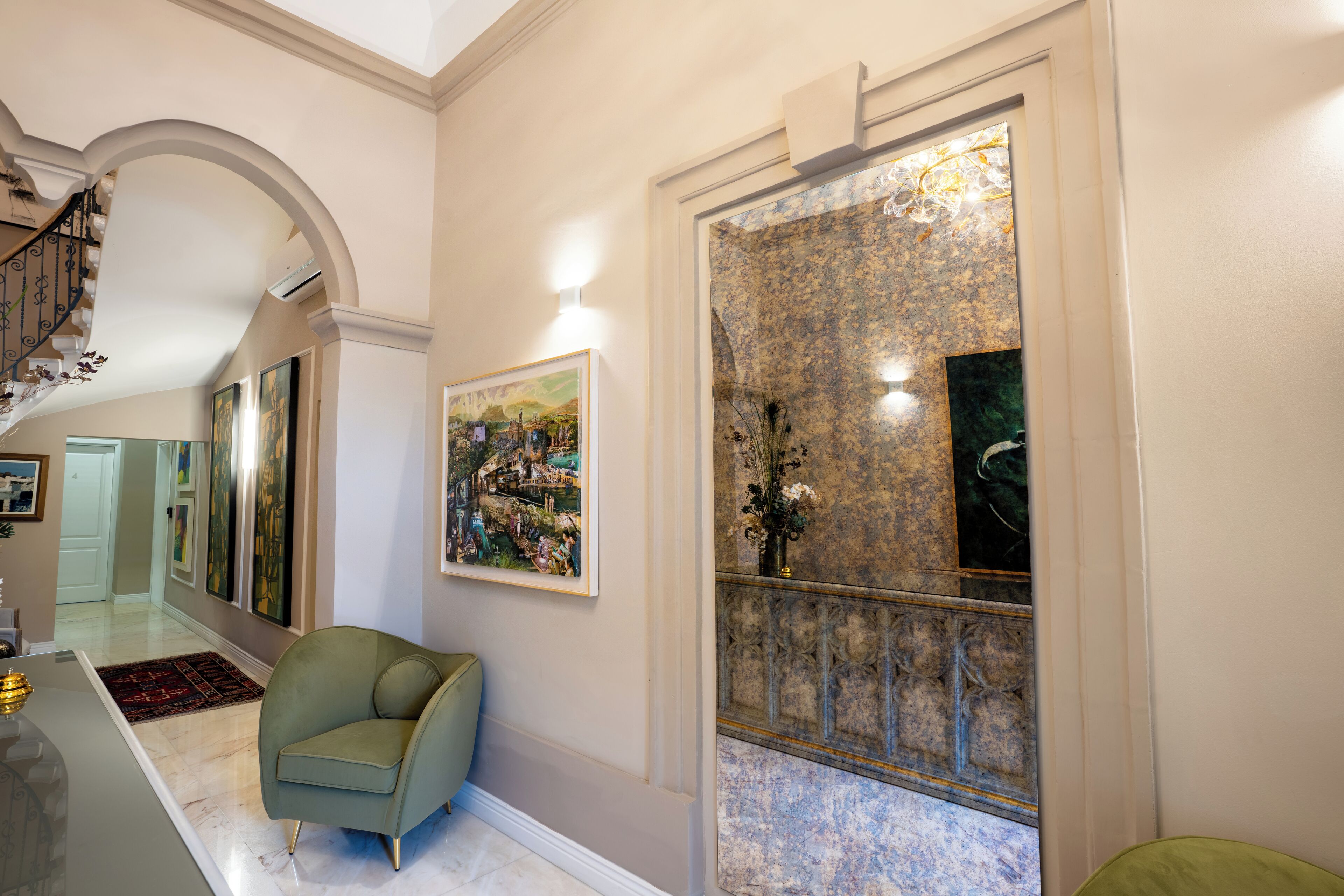 Un couloir avec un fauteuil vert, un tableau encadré et un miroir décoratif.