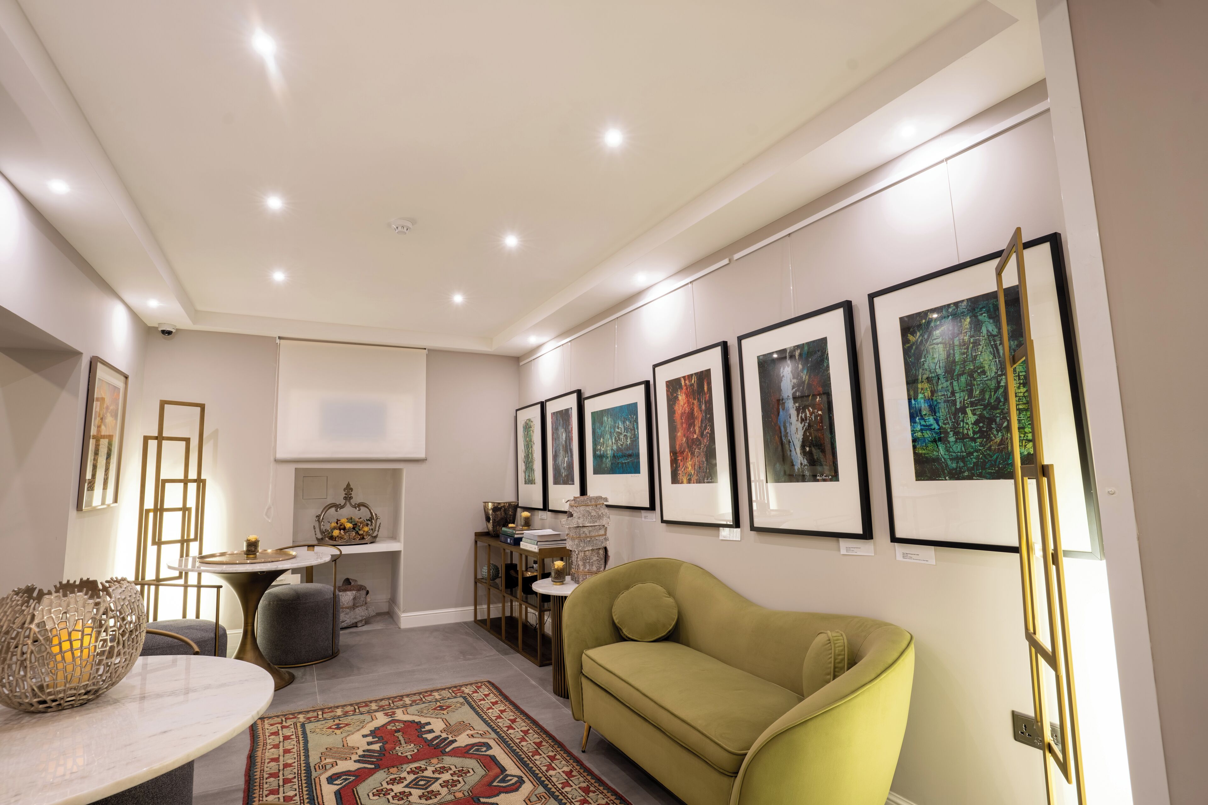 Una sala de estar moderna con un sofá verde, una mesa de centro de mármol y una alfombra estampada. Hay obras de arte enmarcadas en la pared y una pequeña mesita con objetos decorativos.
