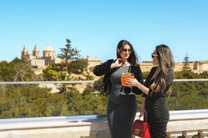 Two individuals on a balcony with a view of a historic building and greenery. - Howard House Hotel (Rabat)