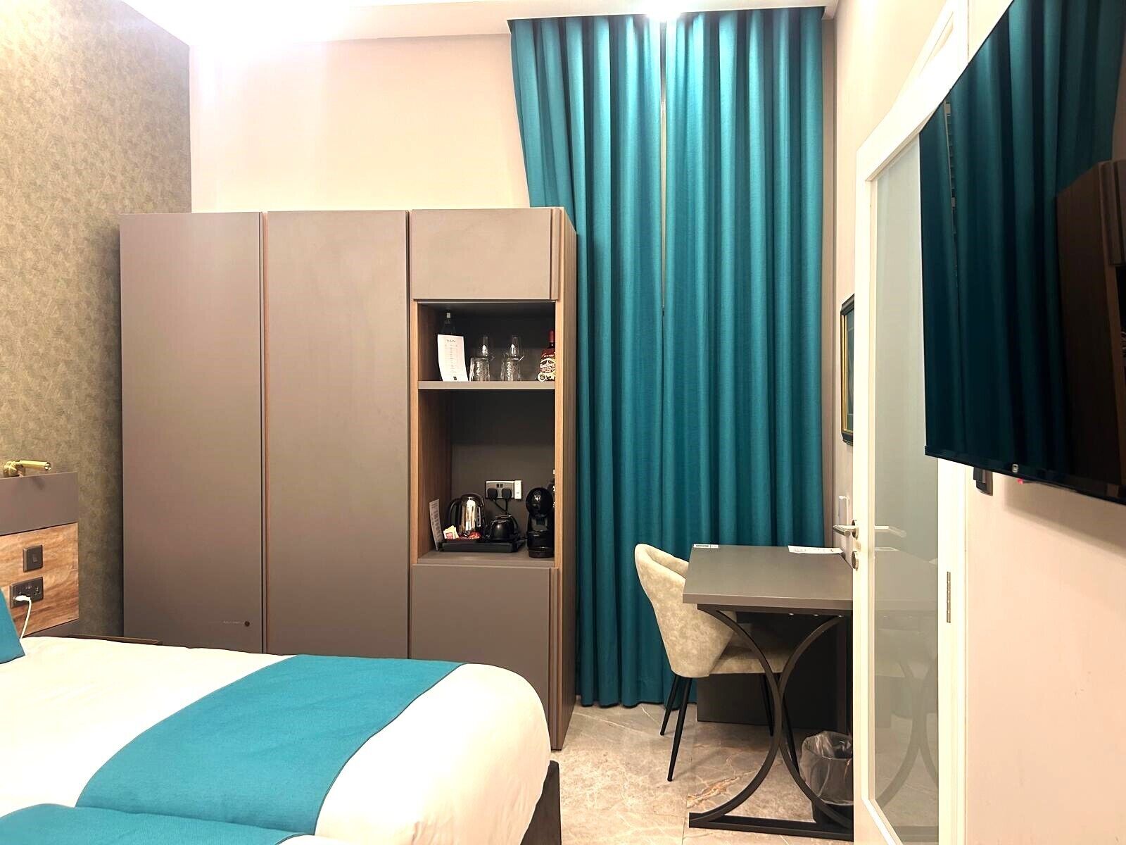 A hotel room with a bed, a desk, a wardrobe, and a television.