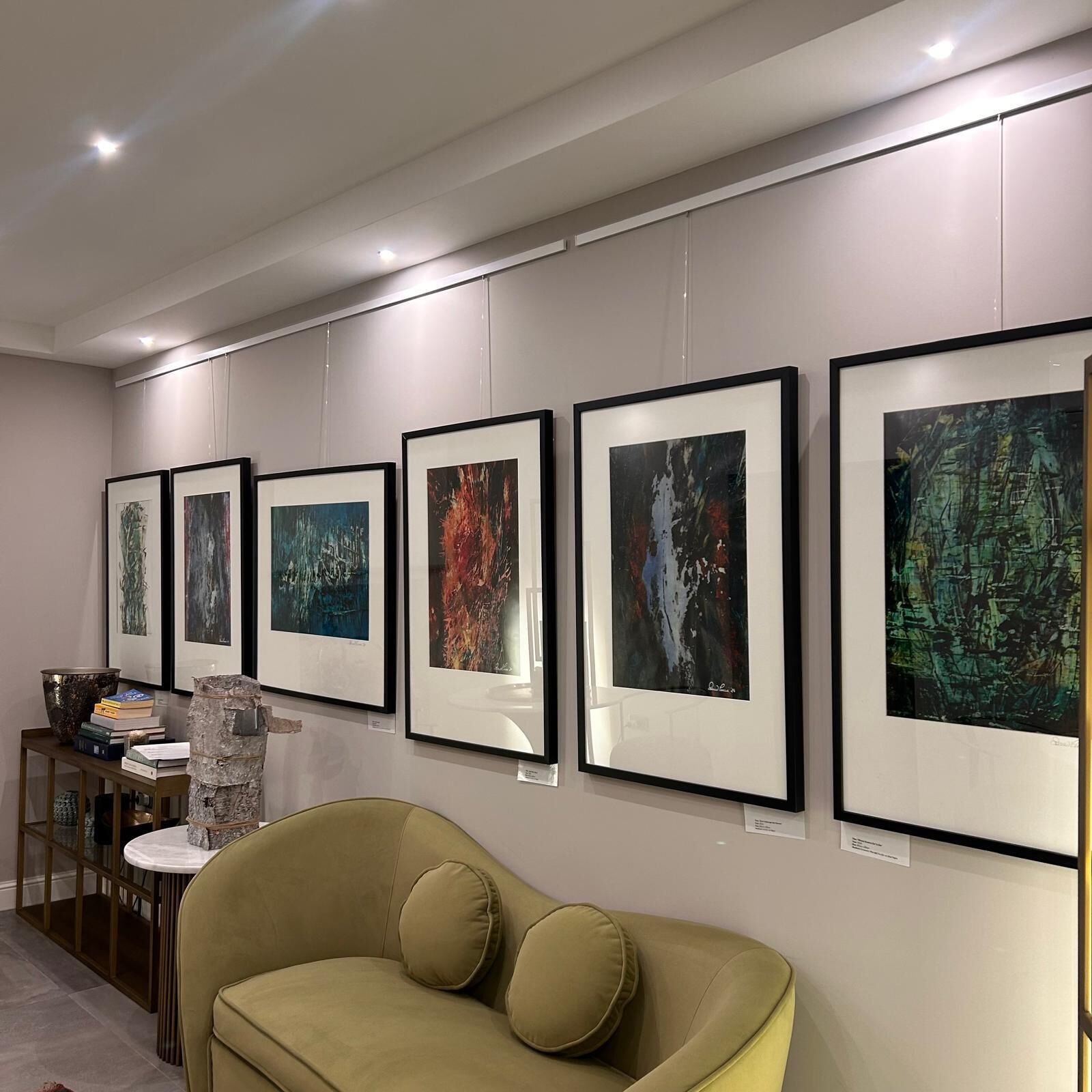 Eine Galerie mit gerahmten Kunstwerken an der Wand, einem Sofa und einem Tisch mit Büchern und einer Skulptur.