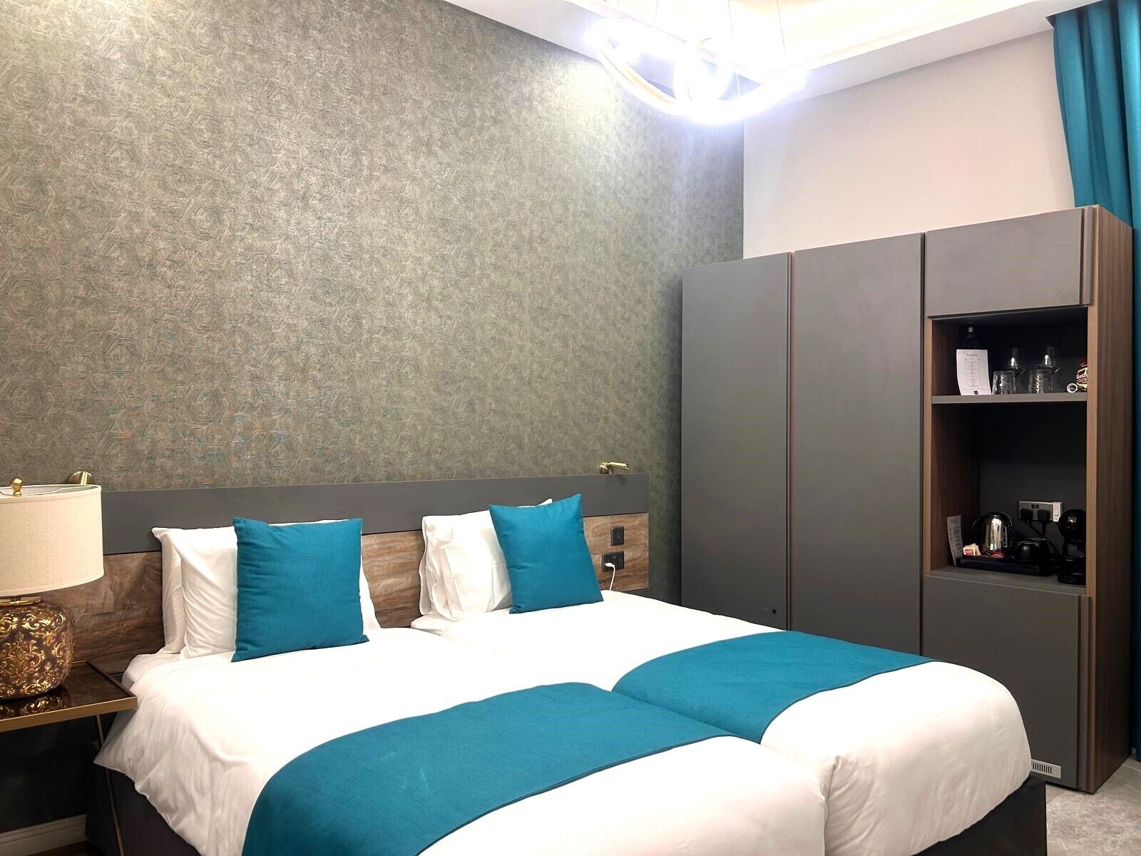 Una habitación de hotel moderna con una cama grande, un armario y una mesita de noche con lámpara.