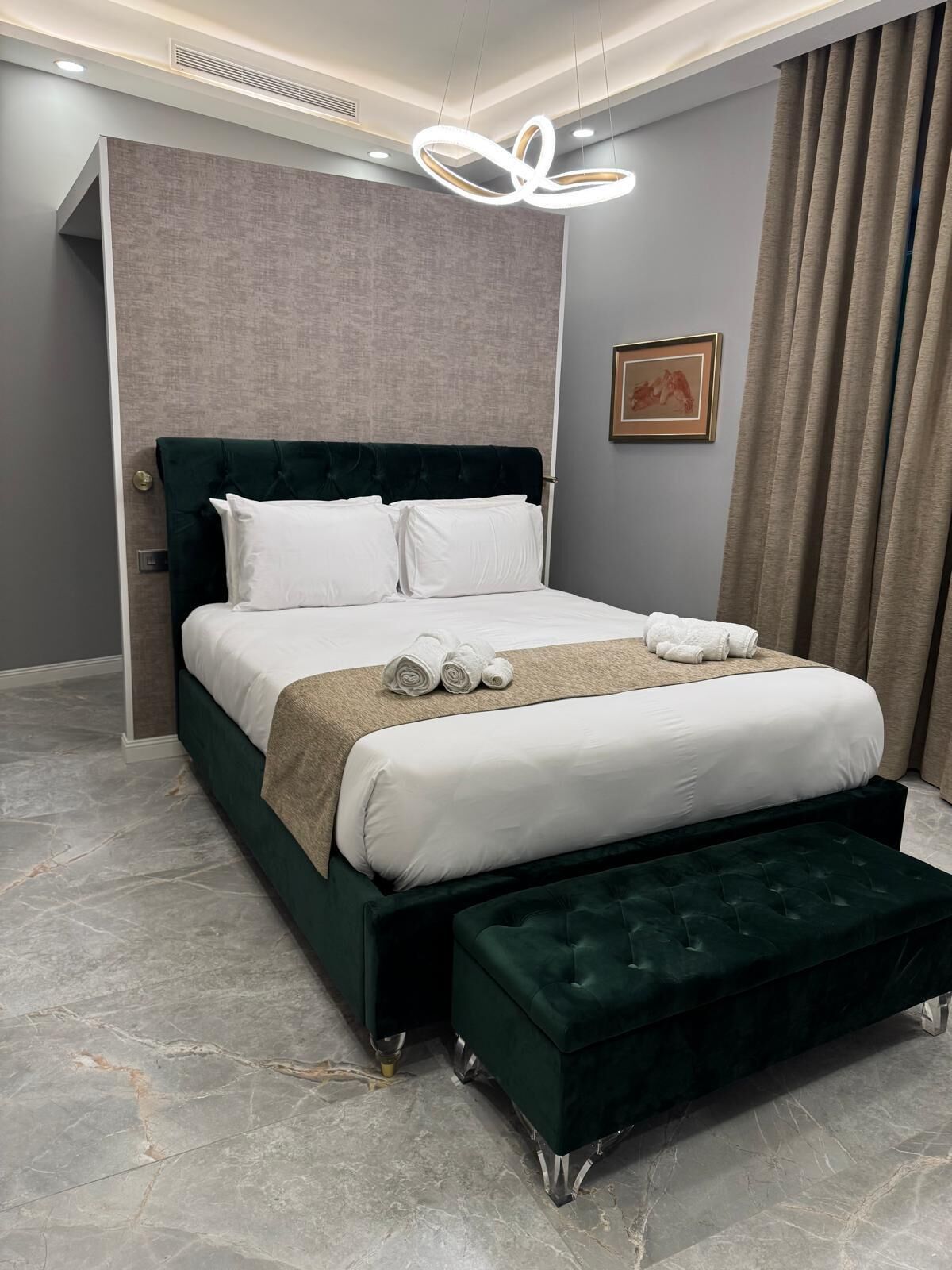 A modern bedroom with a dark green upholstered bed, white bedding, and a marble floor.