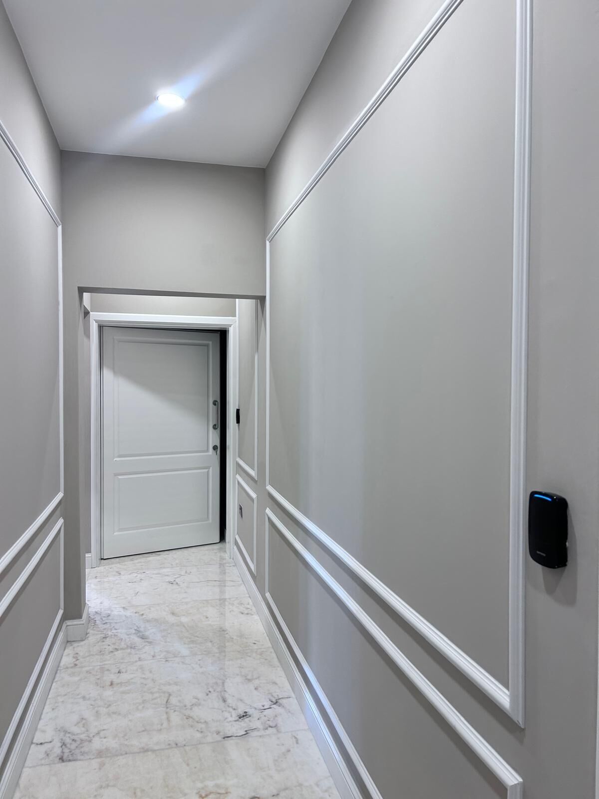 A hallway with a marble floor, white walls, and a door at the end.
