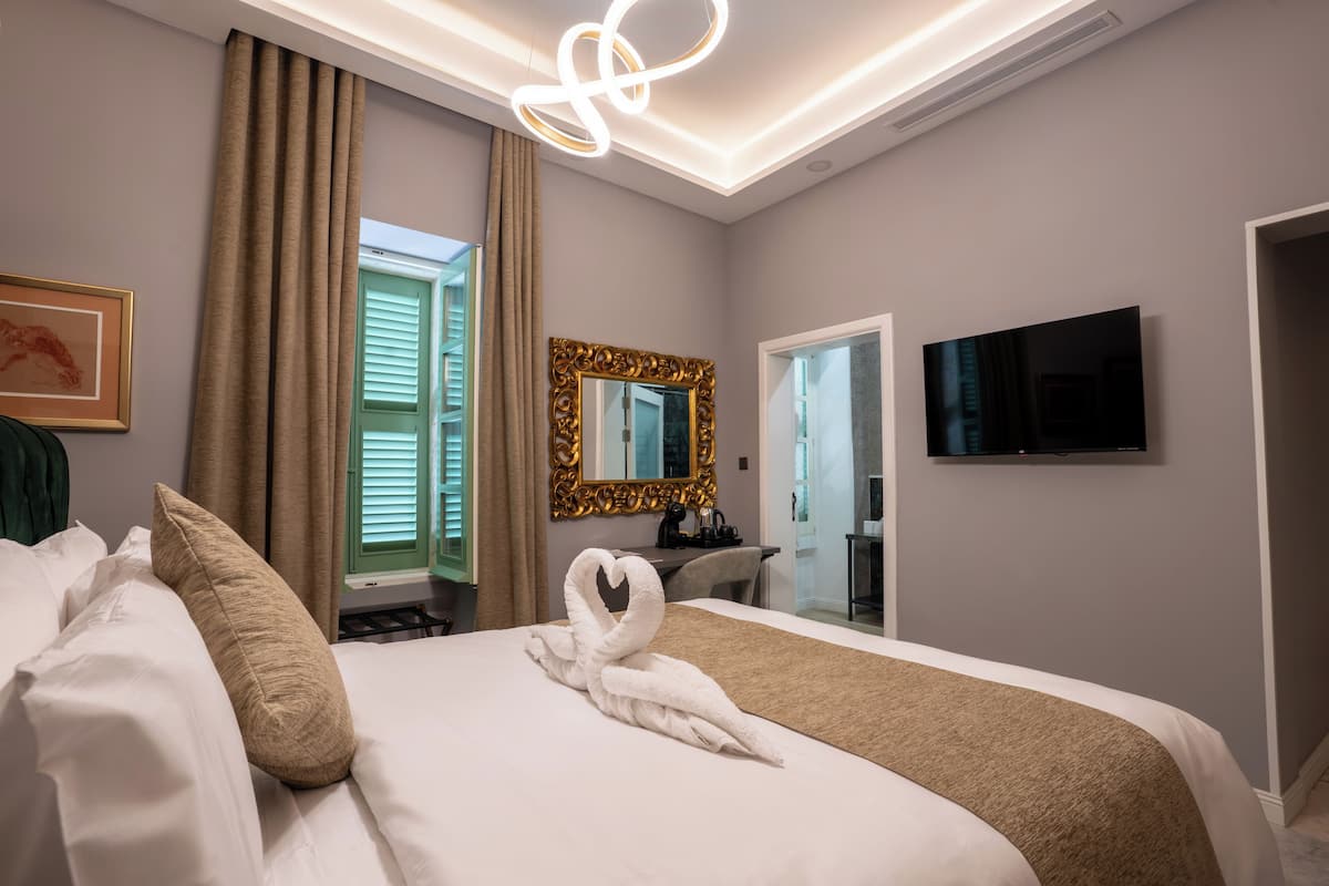 A hotel room with a neatly made bed, a large mirror, a flat-screen TV, and a view of the outside through a window.