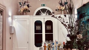 A well-lit hallway with a chandelier, a table with drinks and snacks, and a door with a sign. - Howard House Hotel (Rabat)
