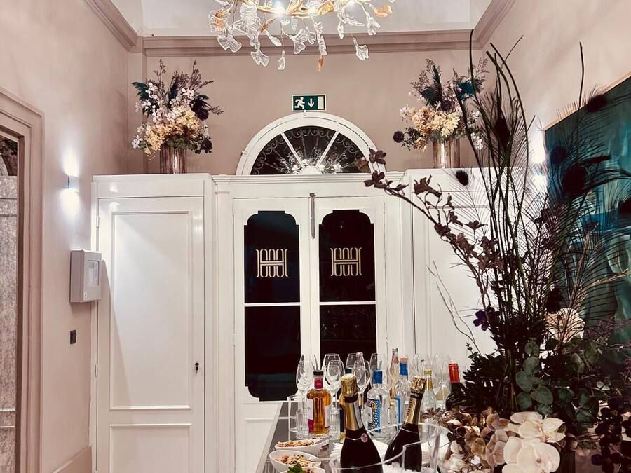 Un pasillo bien iluminado con un candelabro, una mesa con bebidas y aperitivos, y una puerta con un letrero.