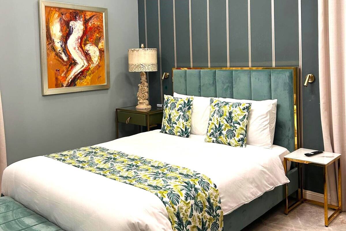 A modern bedroom with a bed, a nightstand, a lamp, a painting, and a ceiling light fixture.