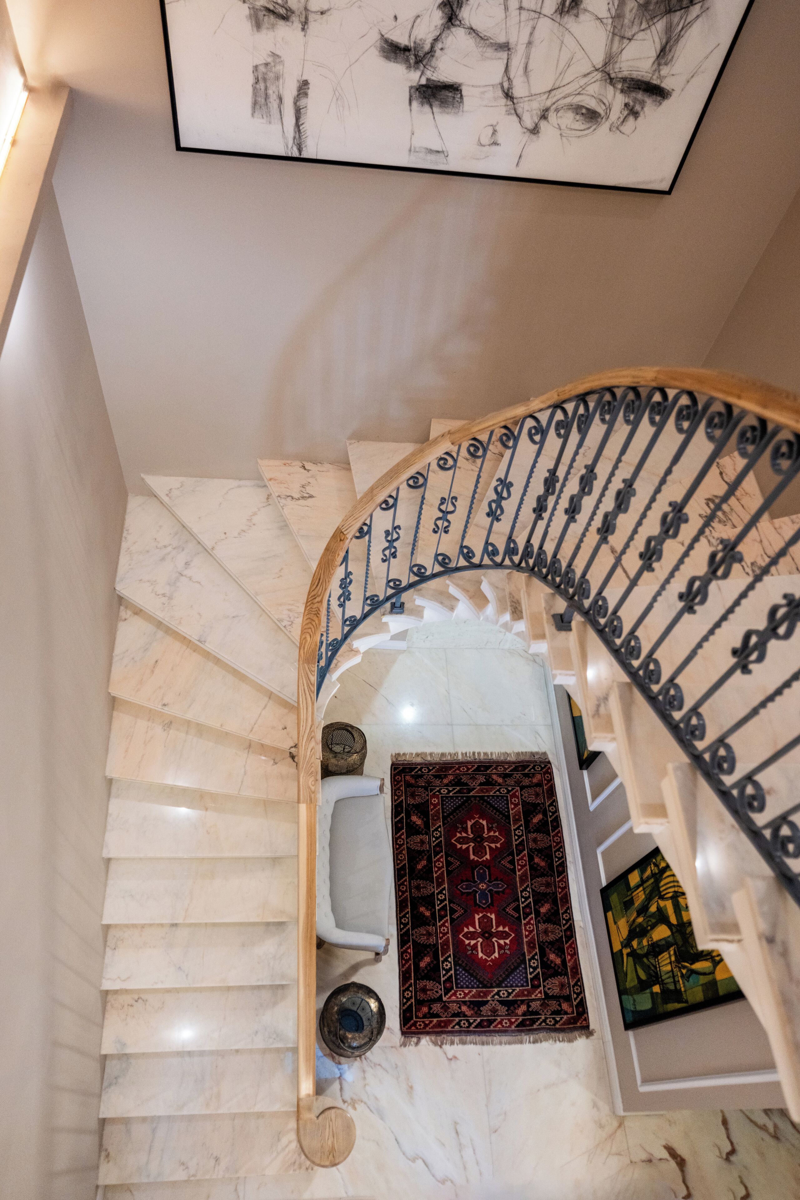 Un escalier en marbre avec une main courante en bois et des balustres en métal noir.