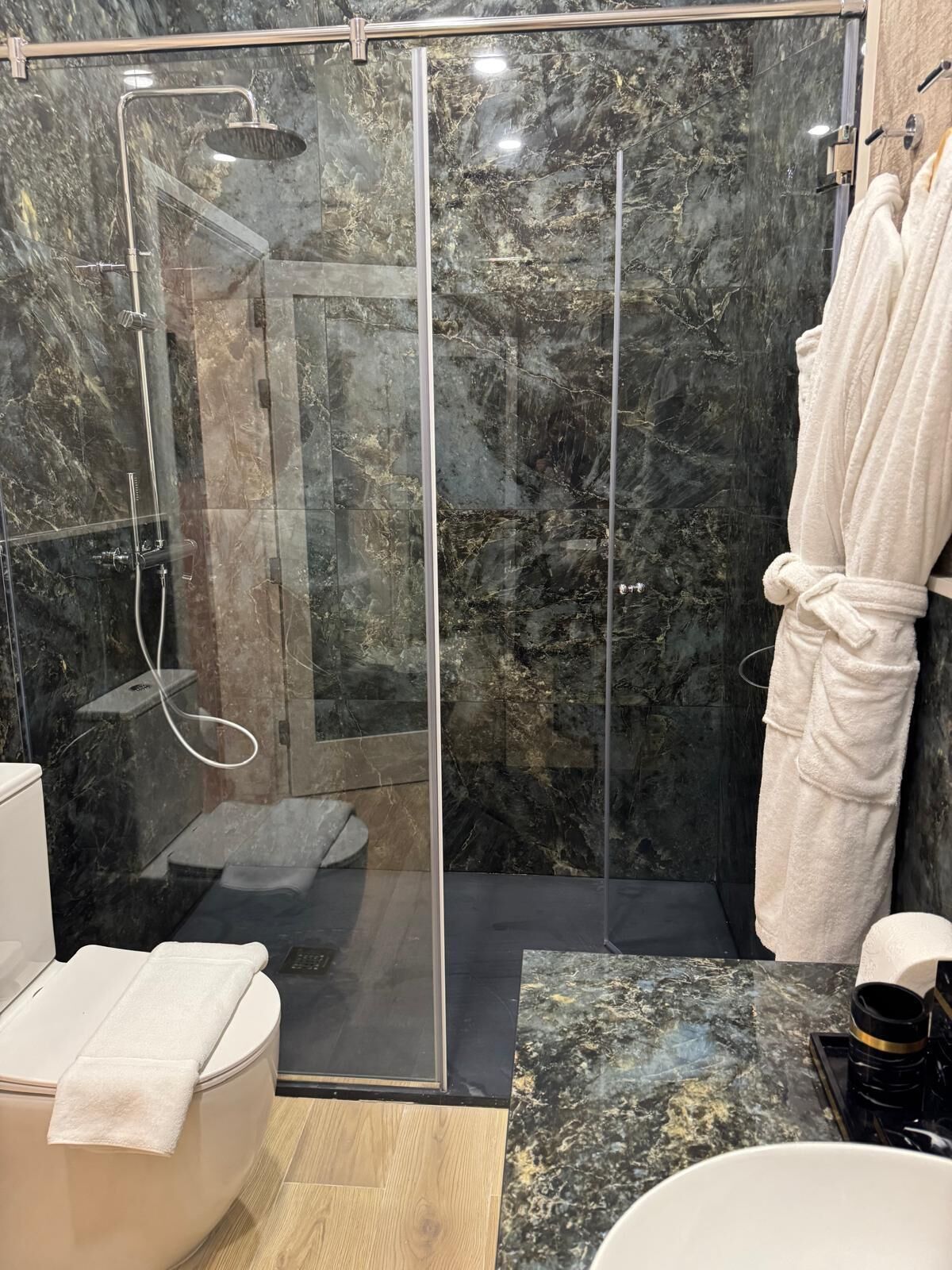 Une salle de bain moderne avec une douche à parois de verre, des murs en marbre et un meuble-lavabo en bois.