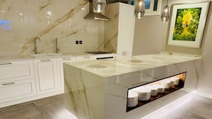 A modern kitchen with a marble countertop, white cabinetry, and a built-in shelf for plates. - Howard House Hotel (Rabat)