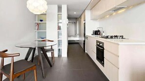 Une cuisine moderne équipée d’une cuisinière à gaz, de meubles blancs et d’un coin repas avec une table et des chaises en verre.