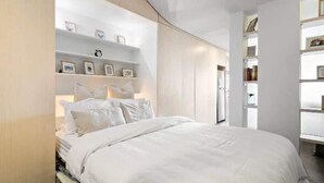 Une chambre moderne avec une tête de lit incurvée, un grand lit et des étagères intégrées ornées de cadres et de livres.