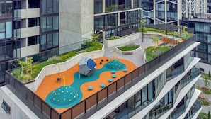 A rooftop garden with play structures, seating areas, and a view of the surrounding buildings. - Luxurious Apartment in Canberra CBD (Reid)