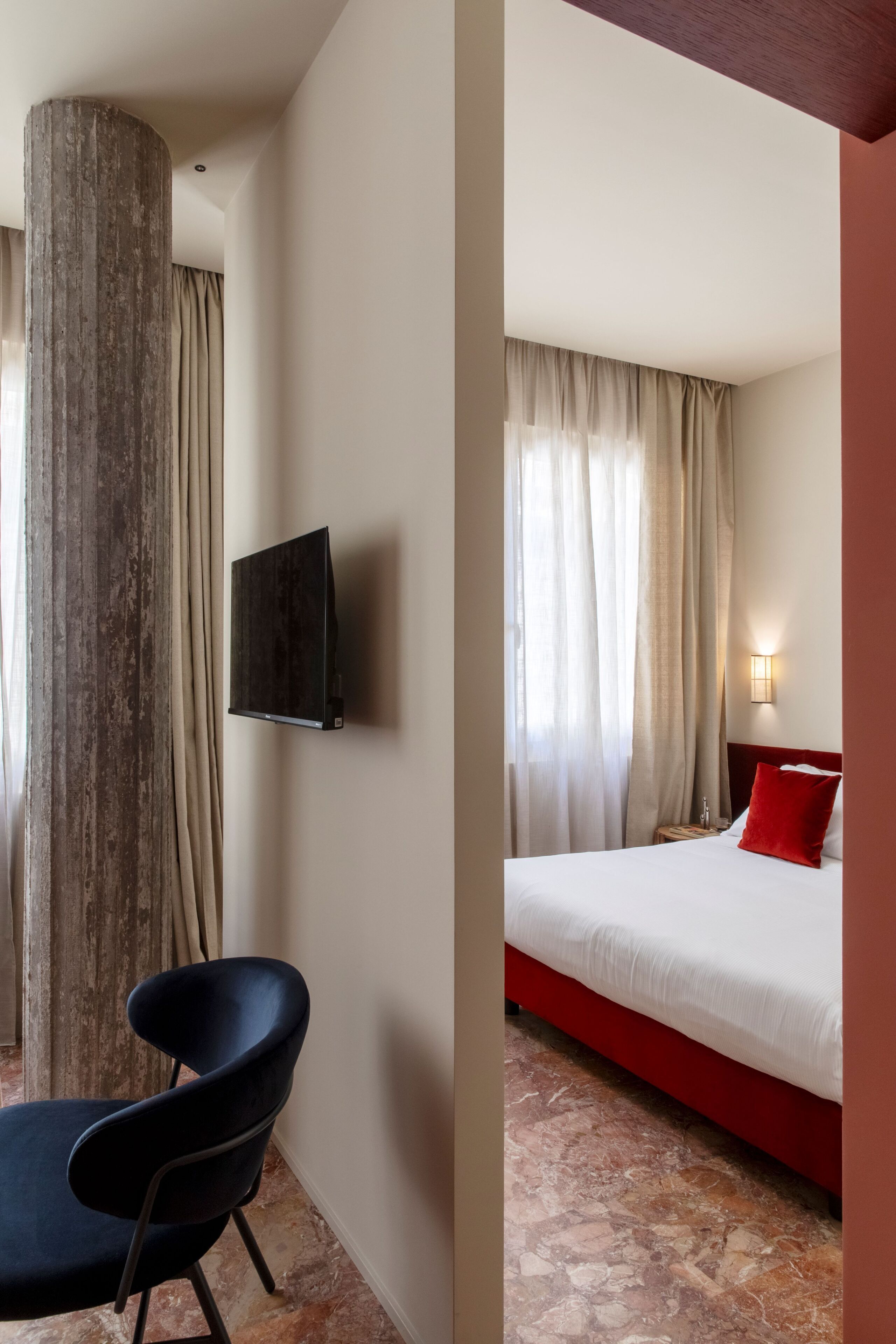 Une chambre d’hôtel avec un lit, un téléviseur fixé au mur, une chaise et une grande colonne.